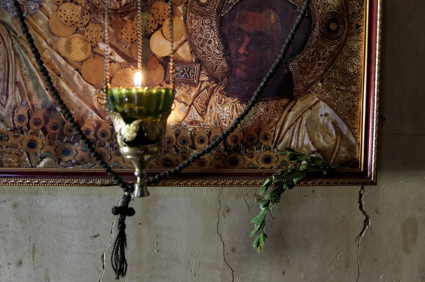 A lit oil vigil lamp with a golden flame burning before a gilded icon, a prayer rope draped beside it.