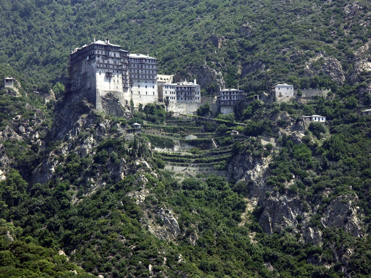 Simonopetra Monastery on the cliffs of Mount Athos, surrounded by green mountains.
