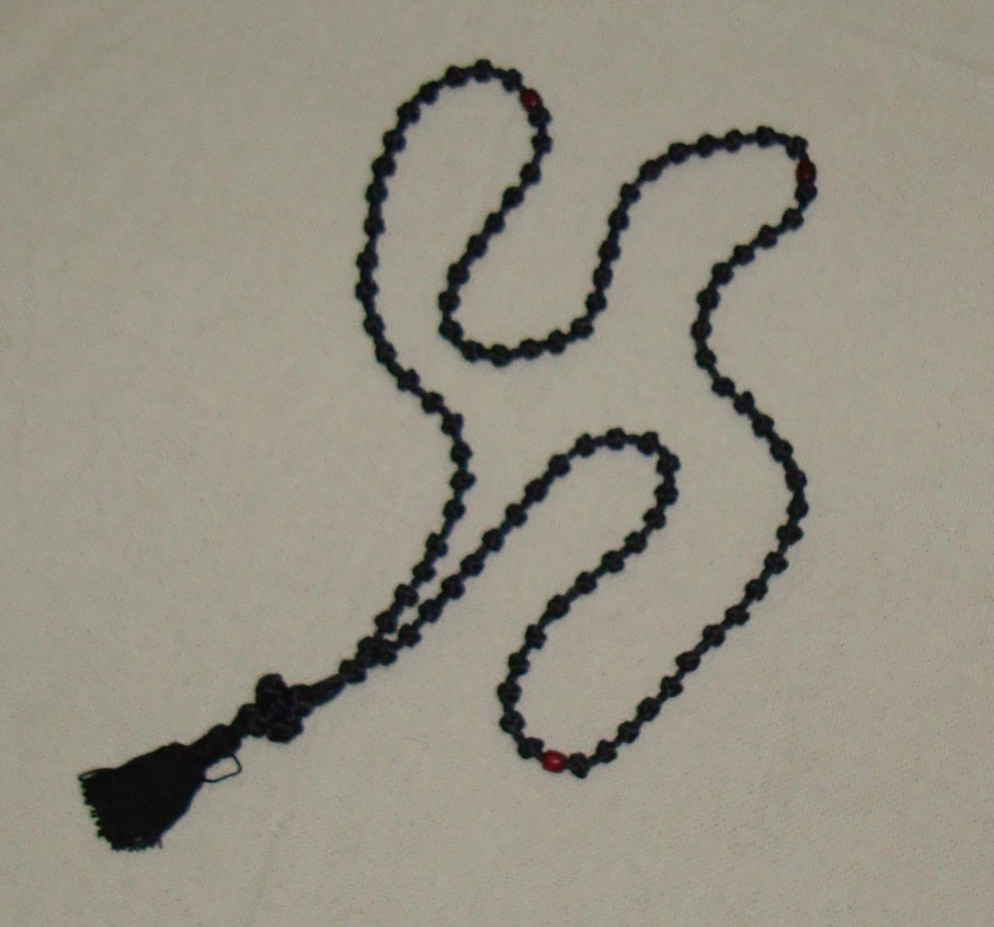 A traditional black wool Orthodox prayer rope with its woven cross, tassel, and red bead dividers, laid in a gentle curve.