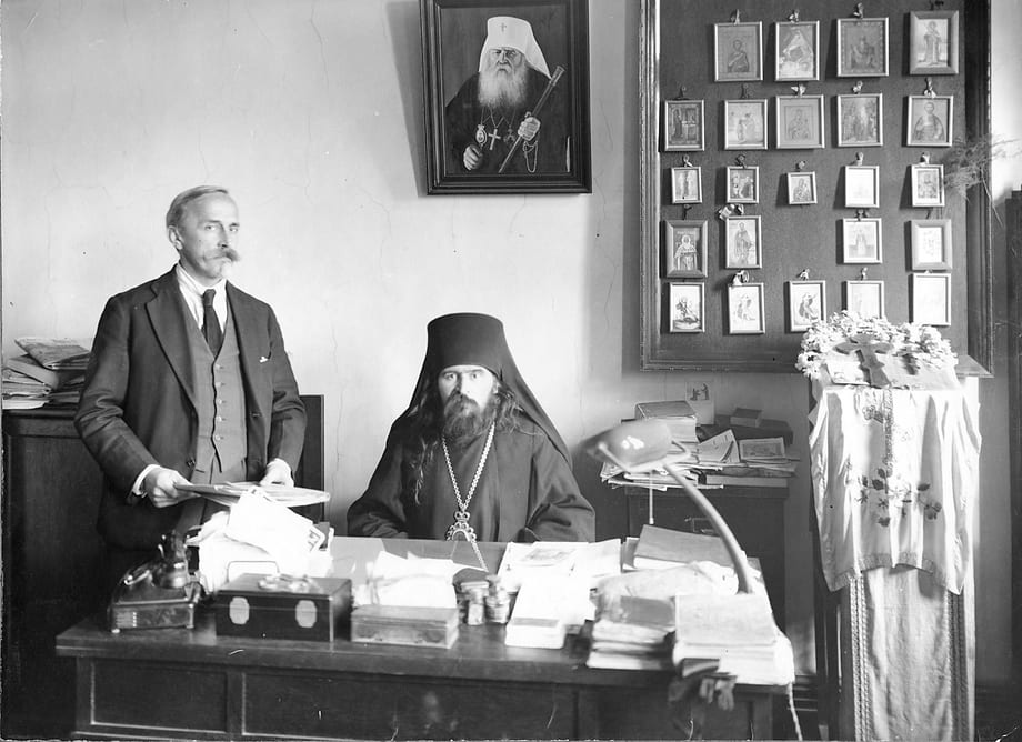 Bishop John seated at his paper-piled desk in his office in Shanghai, China, beneath a portrait of Metropolitan Anthony and a wall of icons
